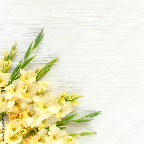 Border frame with yellow gladioluses on wooden white background. Floral pattern of gladioli holiday greeting card. Flat lay  top view. Frame of flowers. Flowers texture