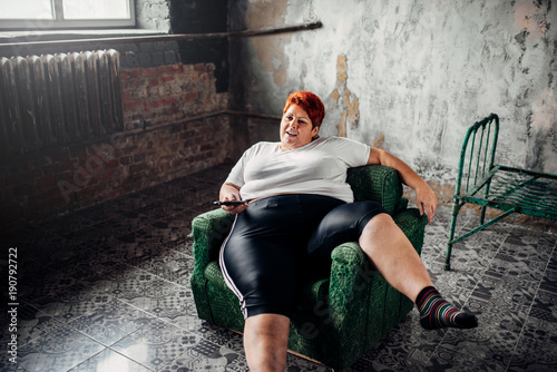 Overweight woman sits in a chair and watches TV