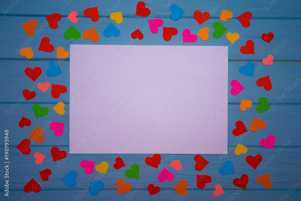 White blank of paper with multicolored hearts around on blue wooden background. Love background. Love concept