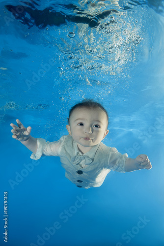 little boy in a costume swims underwater in the pool