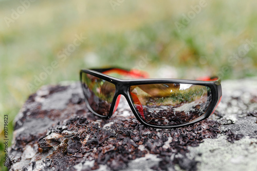Sport male sunglasses on a stone in mountains, travel concept