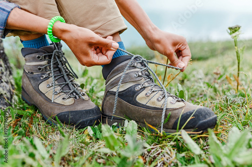 a tourist woman ties up her shoelaces on trekking boots  outdoor footwear concept