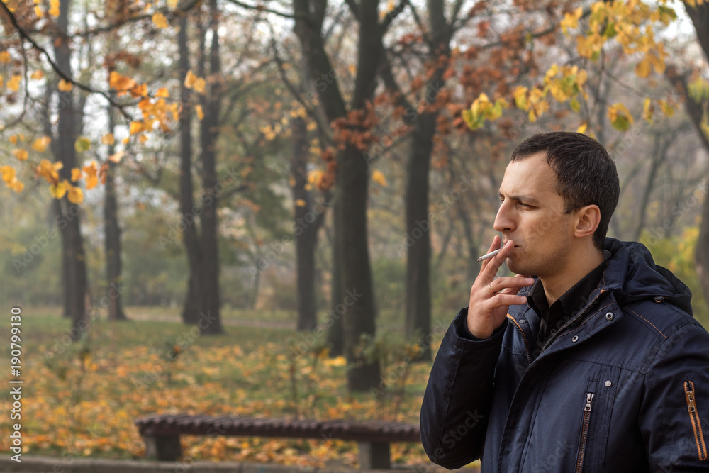 Handsome man walking in the autumn park. Man smoking cigarette in outdoor. Bad habit. Handsome man walking in the autumn park. Man smoking cigarette in outdoor. Bad habit.