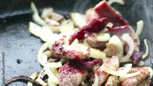 The meat is fried in a pan with onions. The kitchen open-air.