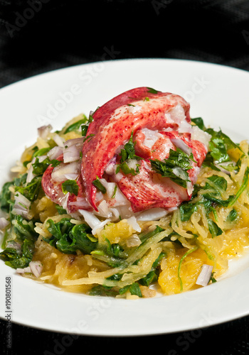 Paleo diet of a tender, roasted lobster with arugula and spaghetti squash on a round, white plate