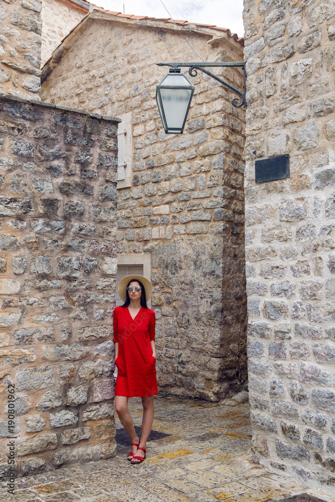 woman in red dress with hat and sunglasses standing in the old town