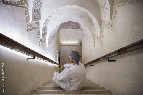 Canvas-taulu arab man in traditional omani outfit in an old castle, sitting on a staircase