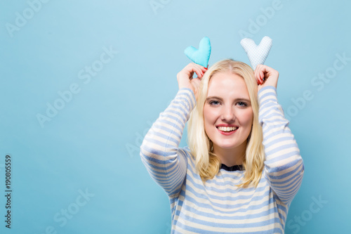 Happy young woman holding heart cushions on a solid background