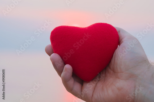 Man hand holding red heart on the beach in sunset