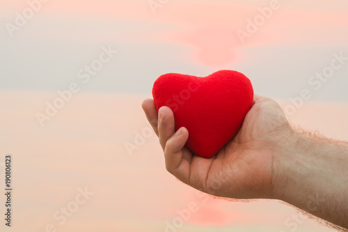 Man hand holding red heart on the beach in sunset