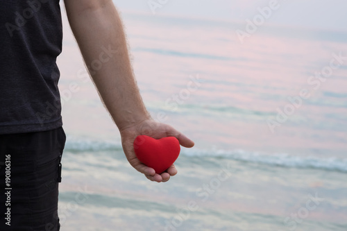 Man hand holding red heart on the beach