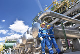 Arbeiter in einer Raffinerie - im Hintergrund Anlage zur Produktion von Treibstoff aus Erdöl - Industrieanlage mit Rohrleitungen // Workers in a refinery - industrial plant with pipelines