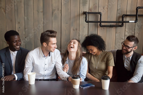 Young man joking at cafe meeting making multiracial friends laugh, diverse people guffaw after guy telling funny comic story during coffee break, happy black and white mates having fun in coffeehouse