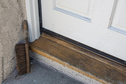 Wood threshold, door and concrete landing of a home with an old shoe brush in corner, horizontal aspect