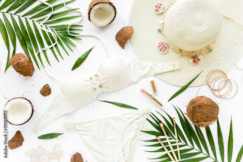 Feminine beige swimsuit beach accessories, tropical palm leaf branches, coconuts on white background. Summer background. Road frame set. Traveler accessories. Flat lay, top view. 