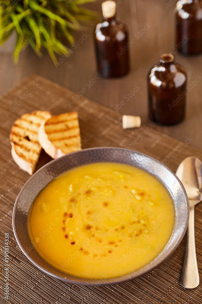 Pumpkin and carrot soup on a brown wooden table. Natural ecological yellow and orange soup puree in a ceramic plate. Healthy meals for lunch with slices of toast bread.