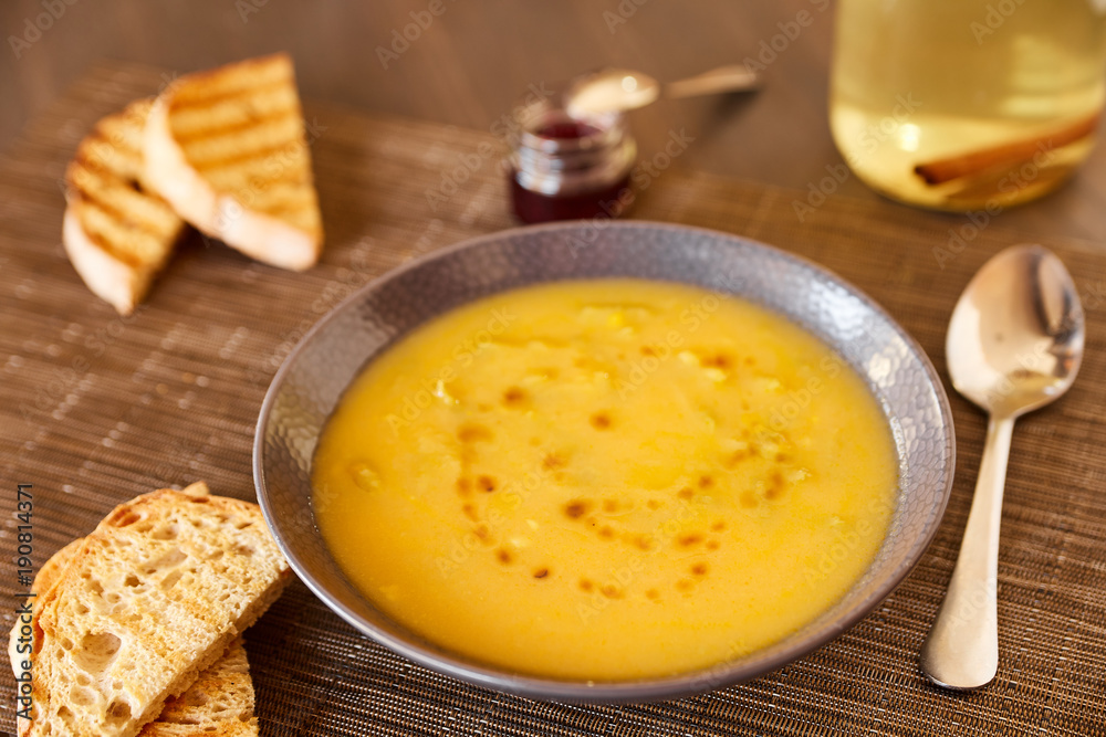 Pumpkin and carrot soup on a brown wooden table. Natural ecological yellow and orange soup puree in a ceramic plate. Healthy meals for lunch with slices of toast bread. Pumpkin and carrot soup on a brown wooden table. Natural ecological yellow and orange soup puree in a ceramic plate. Healthy meals for lunch with slices of toast bread.