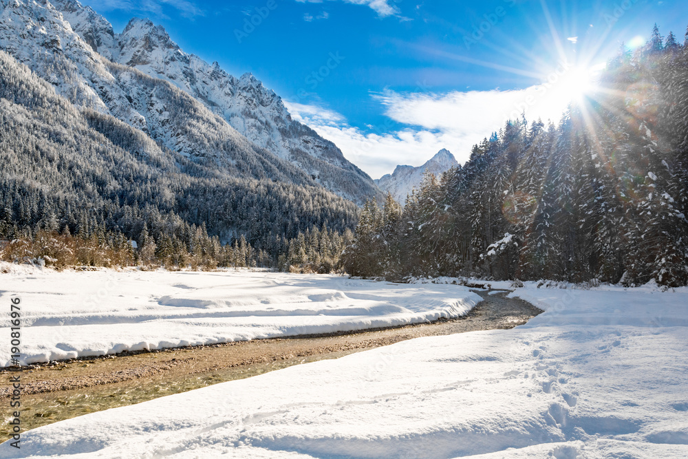 Pisnica creek and setting sun with mountains in the background on a sunny winter day Pisnica creek and setting sun with mountains in the background on a sunny winter day