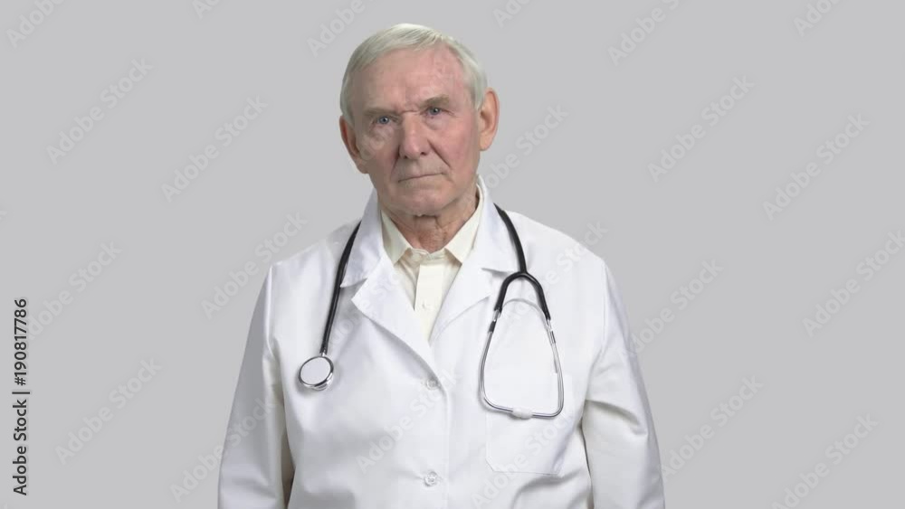 Portrait of serious gloomy face of an old doctor. Frowning old physician in grey isolated background. Portrait of serious gloomy face of an old doctor. Frowning old physician in grey isolated background.
