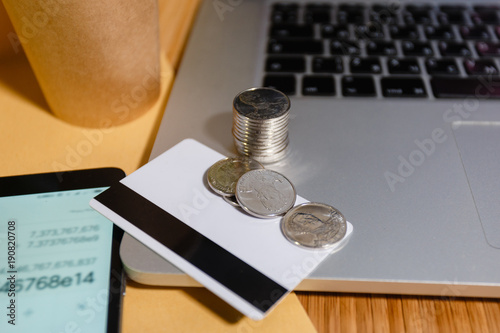 White credit card with the coins on the body panel laptop and smartphone with a calculator application with expense accounts. The concept of calculations personal Finance freelancer