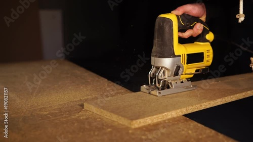Close up shot of a skilled carpenter sawing piece of wood in a workshop. He is using an electric saw. photo
