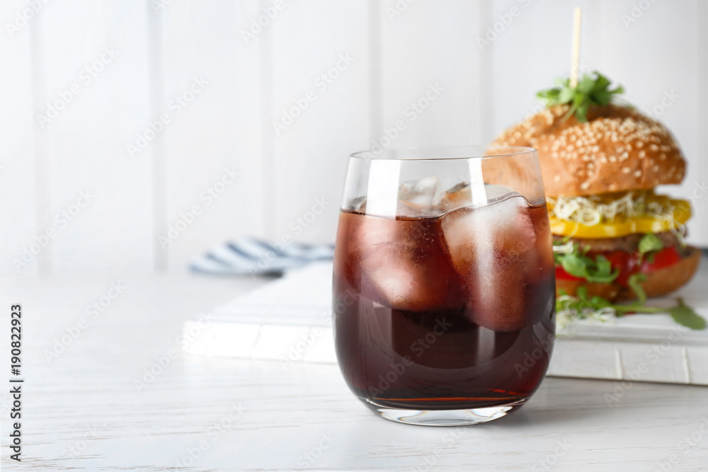 Glass of cold cola with tasty burger on table Glass of cold cola with tasty burger on table