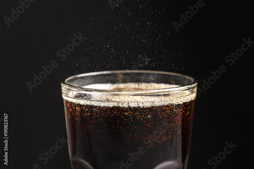 Glass of refreshing cola on black background, closeup