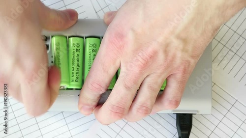 The man inserts a battery into the charger. Green batteries without labels. Full HD video. Renewable Energy Storage. Hands close-up top. Lit red LEDs.