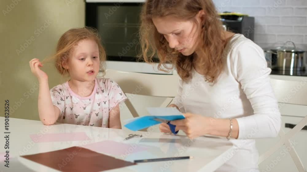 A woman with a girl doing an application of colored paper sitting at a table at home A woman with a girl doing an application of colored paper sitting at a table at home