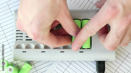 The man inserts a battery into the charger. Green batteries without labels. Full HD video. Renewable Energy Storage. Hands close-up top. Lit red LEDs.