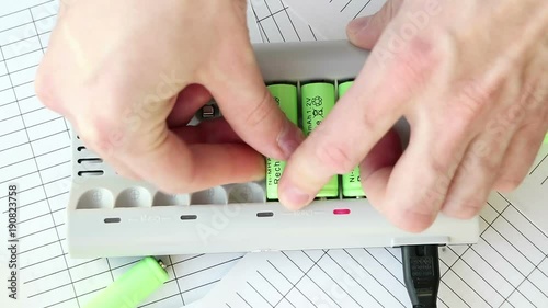 The man inserts a battery into the charger. Green batteries without labels. Full HD video. Renewable Energy Storage. Hands close-up top. Lit red LEDs. Speed-up view.