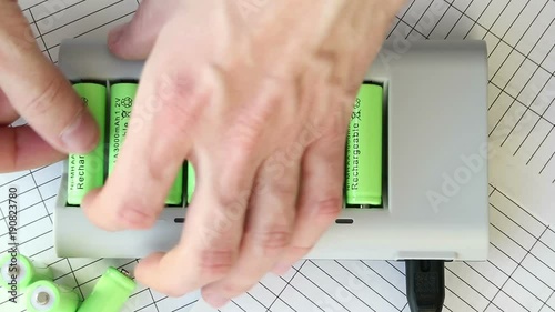 The man inserts a battery into the charger. Green batteries without labels. Full HD video. Renewable Energy Storage. Hands close-up top. Lit red LEDs. Speed-up view.