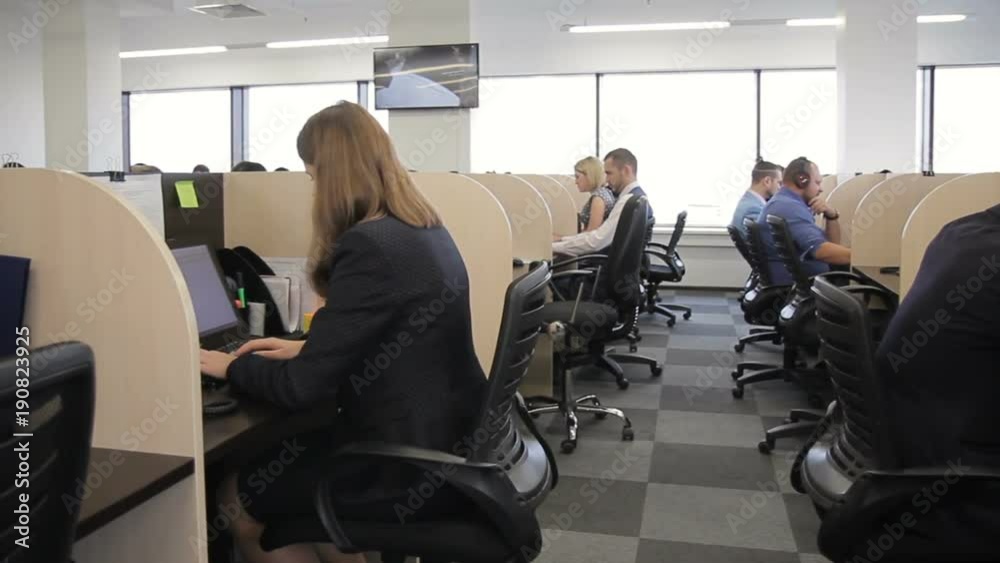 Work team works, sitting at tables with computers in large company. Men and women are engaged in working affairs, looking at PC screens, locating at individual workplaces separated by partitions