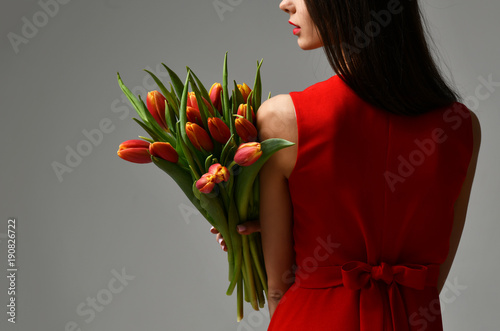Beautiful woman with bouquet of tulip flowers in red dress and little sticker on tulips 