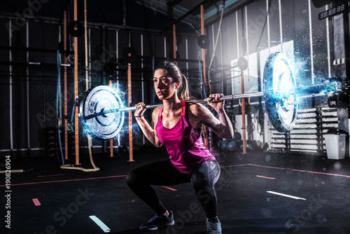 Athletic girl works out at the gym with a barbell with blue energy effects