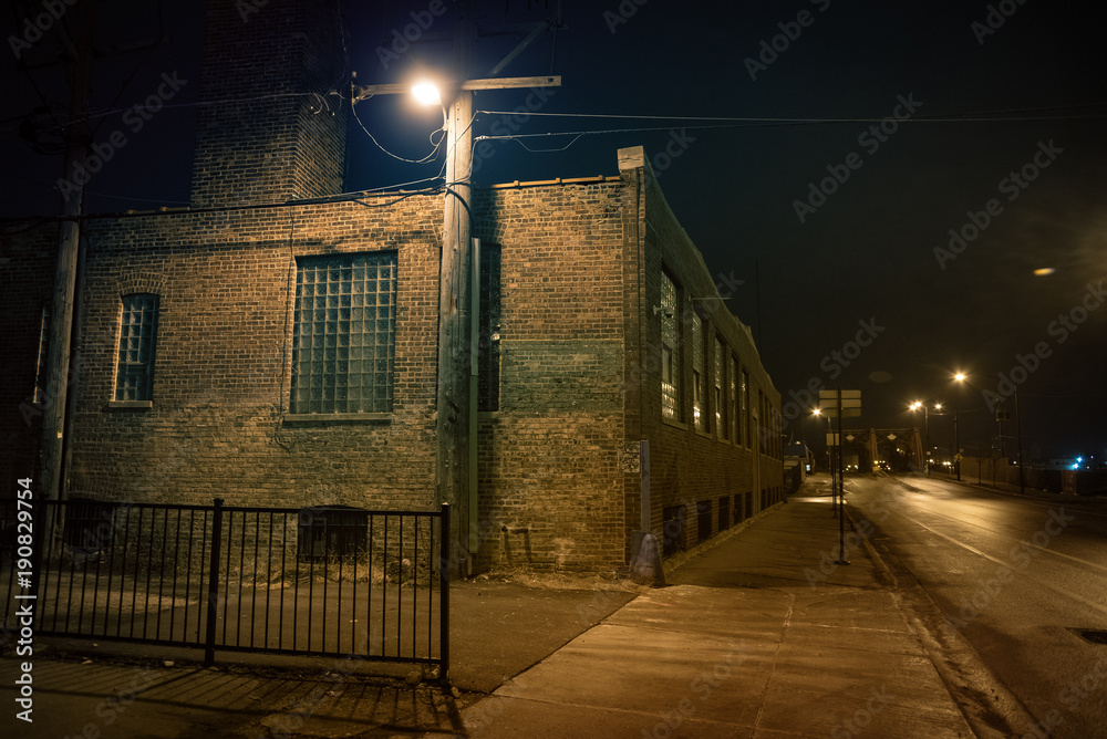 Dark urban city street and alleyway corner with an industrial warehouse  factory and an urban road leading to a vintage bridge in Chicago at night.  Stock Photo | Adobe Stock