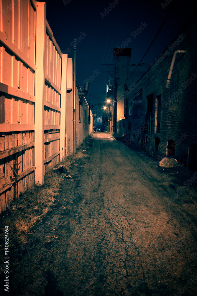 Dark and eerie urban city alley with an old vintage factory warehouse and smokestack at night.