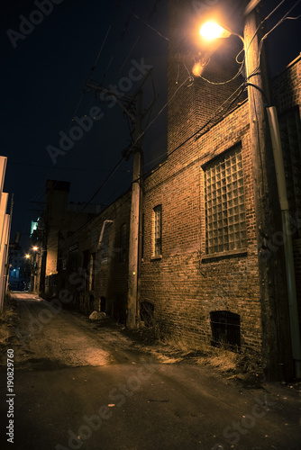Dark and eerie urban city alley with an old vintage factory warehouse and smokestack at night.