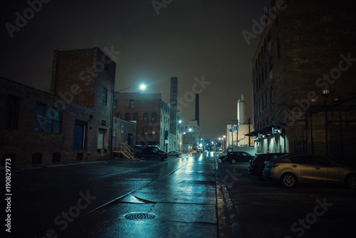Foggy industrial urban street city night scenery in Chicago with vintage warehouses, factories and smokestacks after a rain.