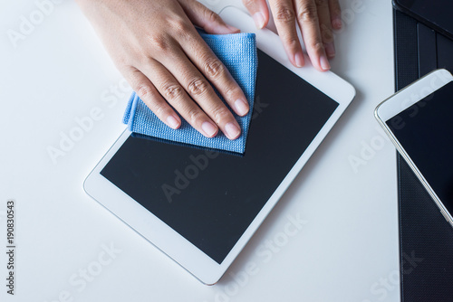 Hand female cleaning dirty her tablet on screen with microfiber cloth photo