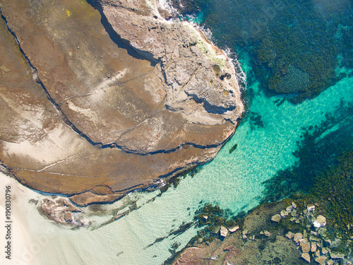 Aerial view of sandy coastline with large granite rock shelf
