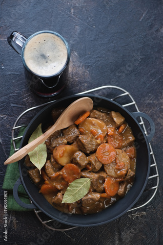 Cast-iron pan with Irish beef and beer stew on a metal cooling rack, high angle view on a dark brown stone background, studio shot
