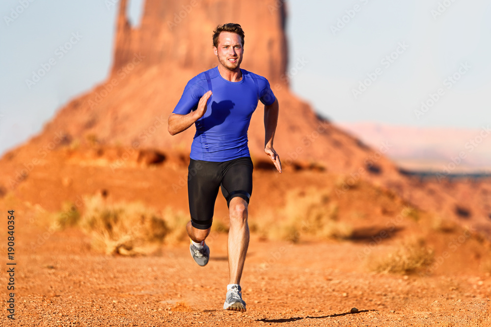 Running man sprinting cross country trail run. Male fit sport fitness model training for marathon outside in beautiful landscape. Caucasian handsome athlele in his 20s.