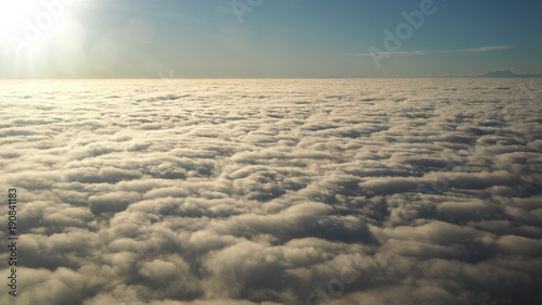 Landscape from the airplane window to a massive sea of clouds in a blue sky