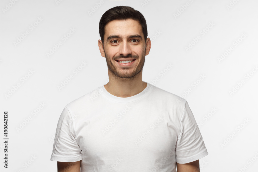 Young smiling optimistic man in blank white t-shirt standing isolated on light gray background Young smiling optimistic man in blank white t-shirt standing isolated on light gray background