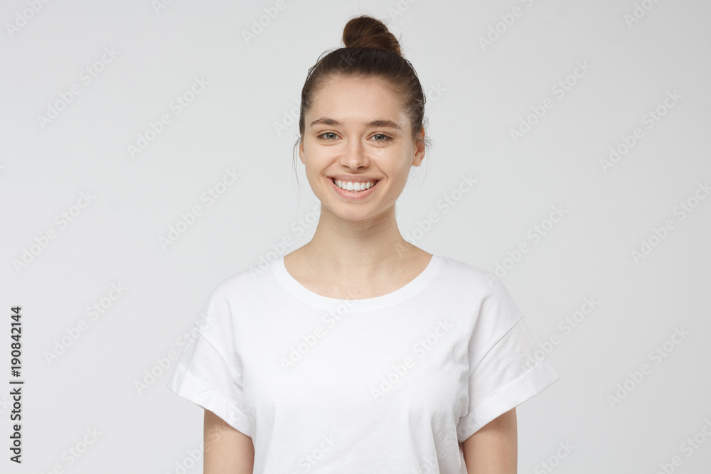 Close up portrait of smiling young woman in white t-shirt looking at camera, isolated on gray background Close up portrait of smiling young woman in white t-shirt looking at camera, isolated on gray background