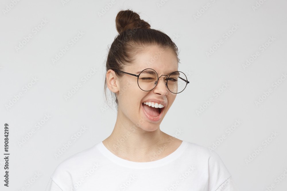 Young woman in round spectacles smiling and winking, looking at camera Young woman in round spectacles smiling and winking, looking at camera
