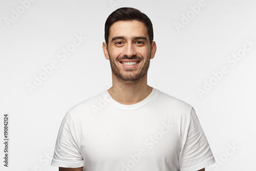 Close up portrait of smiling handsome man in white t-shirt looking at camera, isolated on gray background