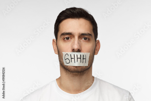 Close up shot of young man with taped mouth with shhh text on it