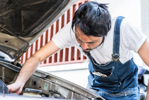 Fixing car engine in automobile repair garage. Handsome mechanics in uniform are repairing car while working in auto service